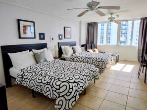 A hotel room with two beds, a ceiling fan, a window with curtains, and framed pictures on the wall. - Luminoso estudio para 4 personas en la playa de Sunny Isles Beach STR-01464 (Sunny Isles Beach)