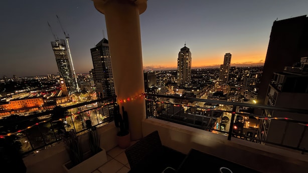A balcony with a city view at dusk, featuring a table, chairs, and a candle.