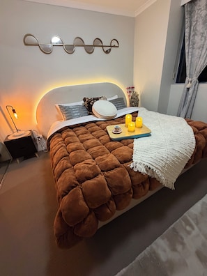 Une chambre à coucher avec une couvre-lit marron à motifs capitonnés, une table de chevet avec une lampe et un luminaire fixé au mur.