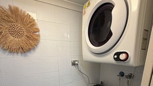 A compact laundry area with a front-loading washing machine and dryer, a wall-mounted dryer, and a decorative wall piece.