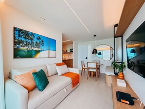 Ein modernes Wohnzimmer mit einer Couch, einem Essbereich mit Tisch und Stühlen, einer Küche im Hintergrund und einem großen Fenster.