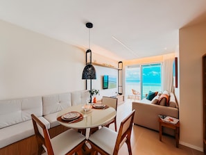A modern living room with a dining area, a sofa, a TV, and a view of the ocean. - Ahead Ponta Negra by Almare (Natal)