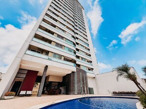 A high-rise hotel with a swimming pool, outdoor seating, and a clear sky. - Ahead Ponta Negra by Almare (Natal)