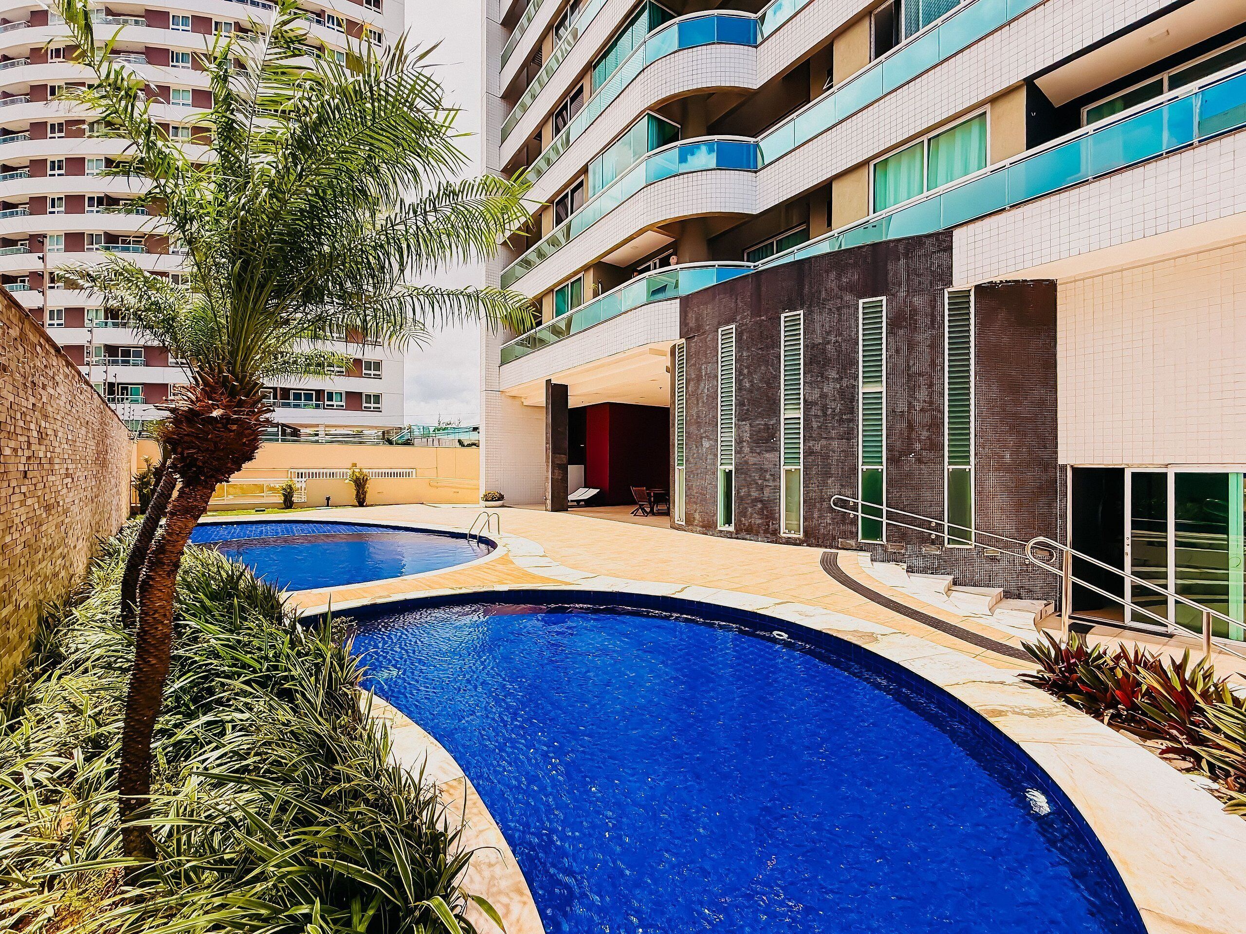 Un edifici modern amb zona de piscina, incloent una piscina corbada i una palmera.