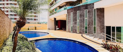A modern building with a pool area, including a curved pool and a palm tree.