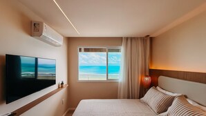 A hotel room with a bed, a flat-screen TV, a window with a view of the ocean, and a wall-mounted air conditioner. - Ahead Ponta Negra by Almare (Natal)