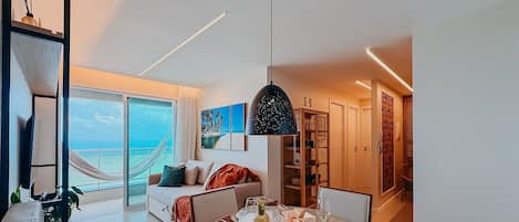 A modern hotel room with a balcony, a dining area, and a view of the sea.