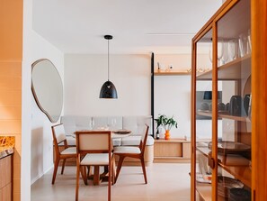 Et moderne spiseområde med et rundt bord, to stole, en hængende pendel og et vitrineskab med service.