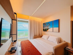A hotel room with a bed, a desk with a computer, a window with a view of the beach, and a painting on the wall. - Ahead Ponta Negra by Almare (Natal)