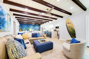 A modern living room with a sofa, ottoman, and a dining area with a kitchen in the background. - Walk To Beach W/Jacuzzi, Perfect for Families! (San Diego)