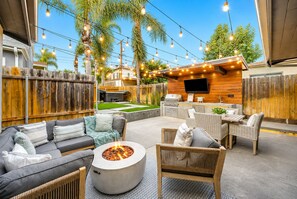 An outdoor patio with a fire pit, seating area, and a TV mounted on a wooden wall. - Walk To Beach W/Jacuzzi, Perfect for Families! (San Diego)