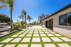 A modern residential area with a paved walkway, palm trees, and a house with large windows. - Walk To Beach W/Jacuzzi, Perfect for Families! (San Diego)