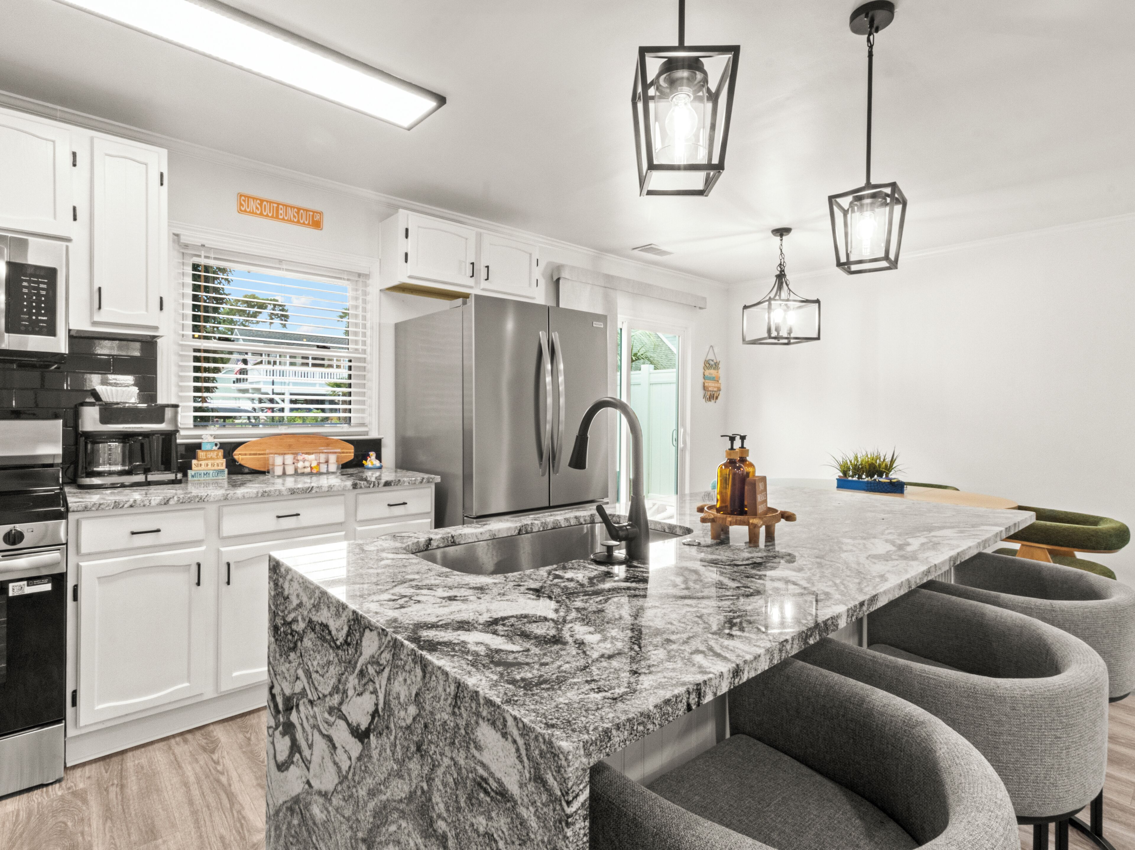 A modern kitchen with white cabinetry, a large island with bar seating, stainless steel appliances, and pendant lighting.
