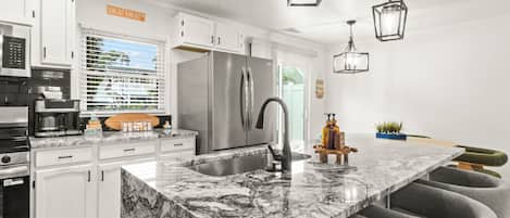 A modern kitchen with white cabinetry, a large island with bar seating, stainless steel appliances, and pendant lighting.