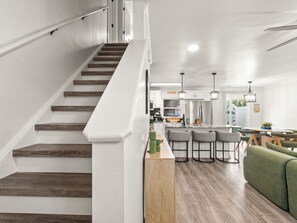 A modern kitchen with wooden flooring, a bar area with stools, and a staircase with wooden steps. - Private Home l 5 min Walk to Beach l 3BR l Pool (North Myrtle Beach)