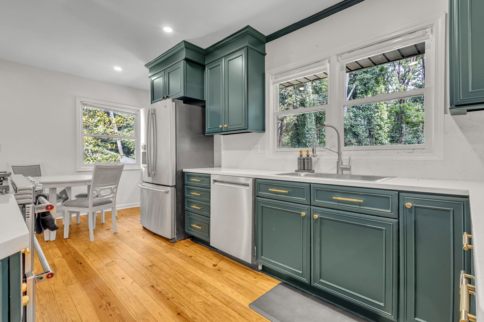 A modern kitchen with wooden flooring, green cabinets, and a built-in refrigerator.