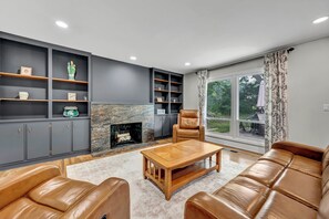 A modern living room with a fireplace, leather furniture, and a view of the outdoors.