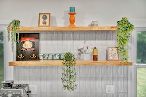 A kitchen shelf with a coffee advertisement, a framed menu, a decorative candle, and hanging plants. - The Spartan Ranch (East Lansing)