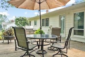 An outdoor patio with a round glass table and four chairs, an umbrella, and a grill. - The Spartan Ranch (East Lansing)