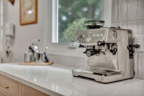 Een koffieapparaat op een aanrecht, met een raam op de achtergrond.