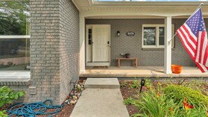 A residential house with a brick exterior, a front door, a mailbox, and an American flag. - The Spartan Ranch (East Lansing)