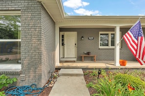 A residential house with a brick exterior, a front door, a mailbox, and an American flag. - The Spartan Ranch (East Lansing)