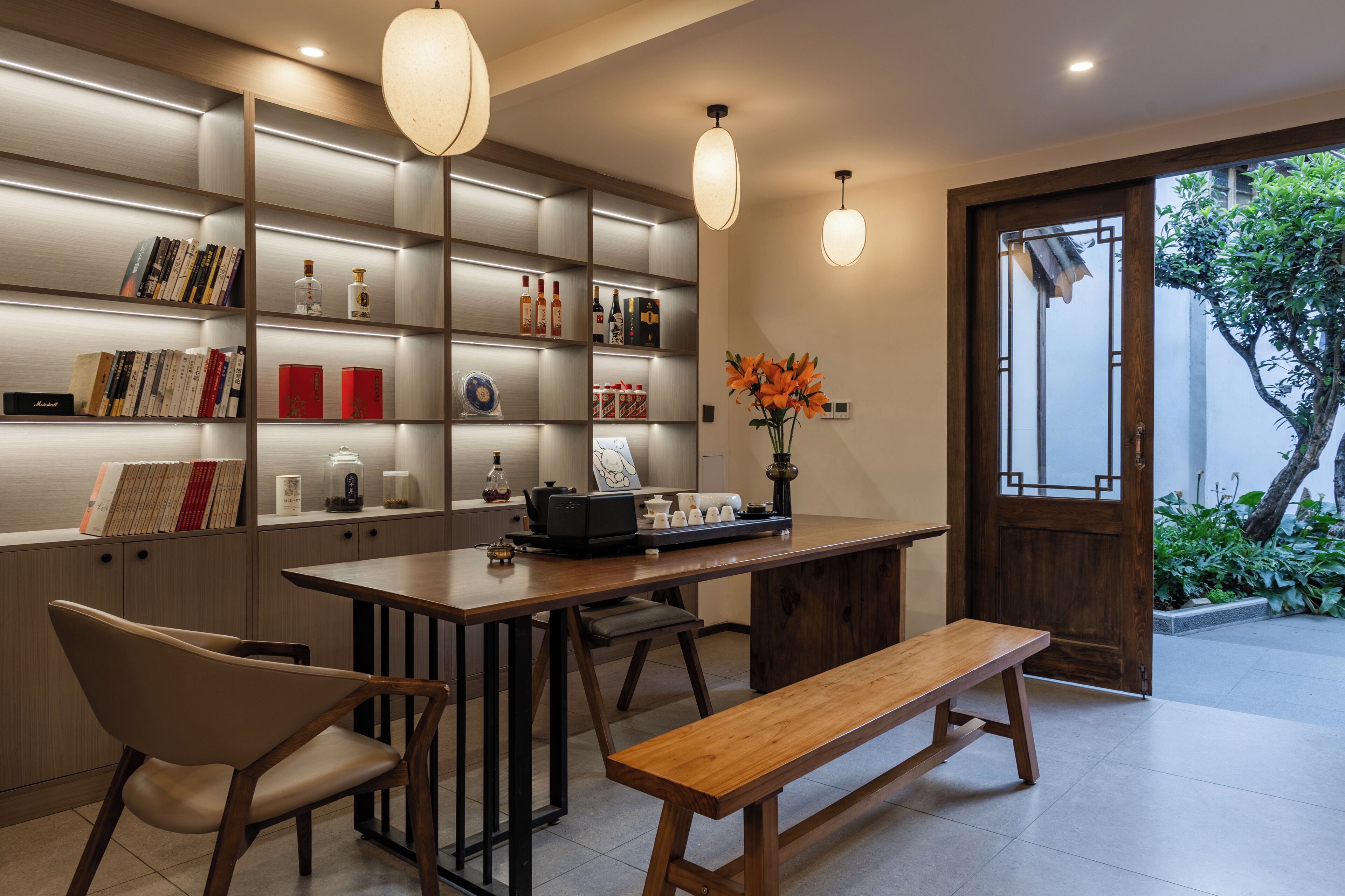 A modern interior with a wooden dining table, chairs, and a bench. There are shelves with books and decorative items.