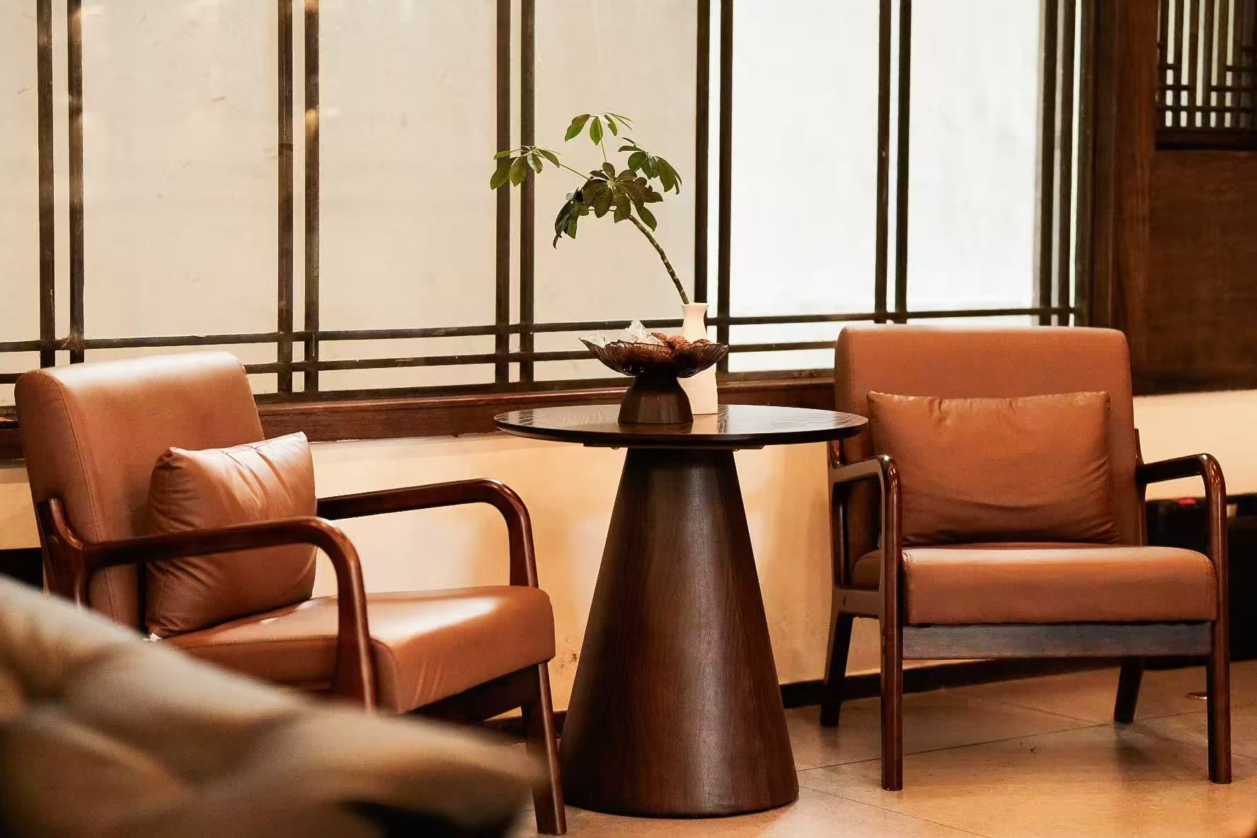 A seating area with leather chairs and a round table, a potted plant, and a window with vertical blinds.