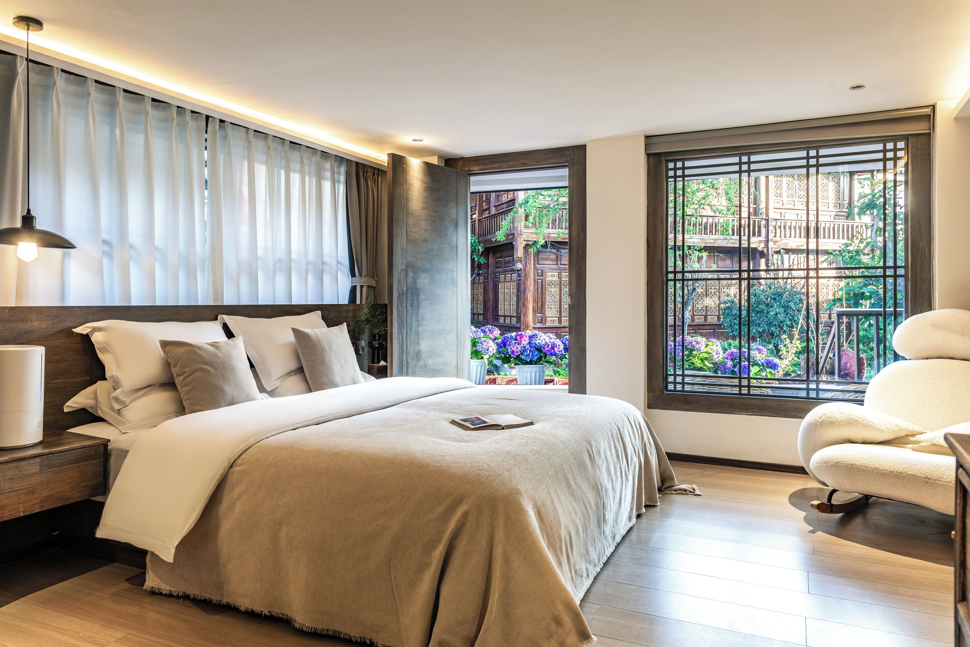 Une chambre moderne avec un grand lit, une table de chevet, une lampe de chevet et une vue sur un jardin par la fenêtre.