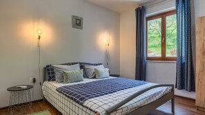 A bedroom with a bed, two bedside lamps, a small table, and a window with curtains.