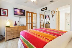 Une chambre à coucher comprenant un lit, un téléviseur, une commode et une porte donnant sur une autre pièce.
