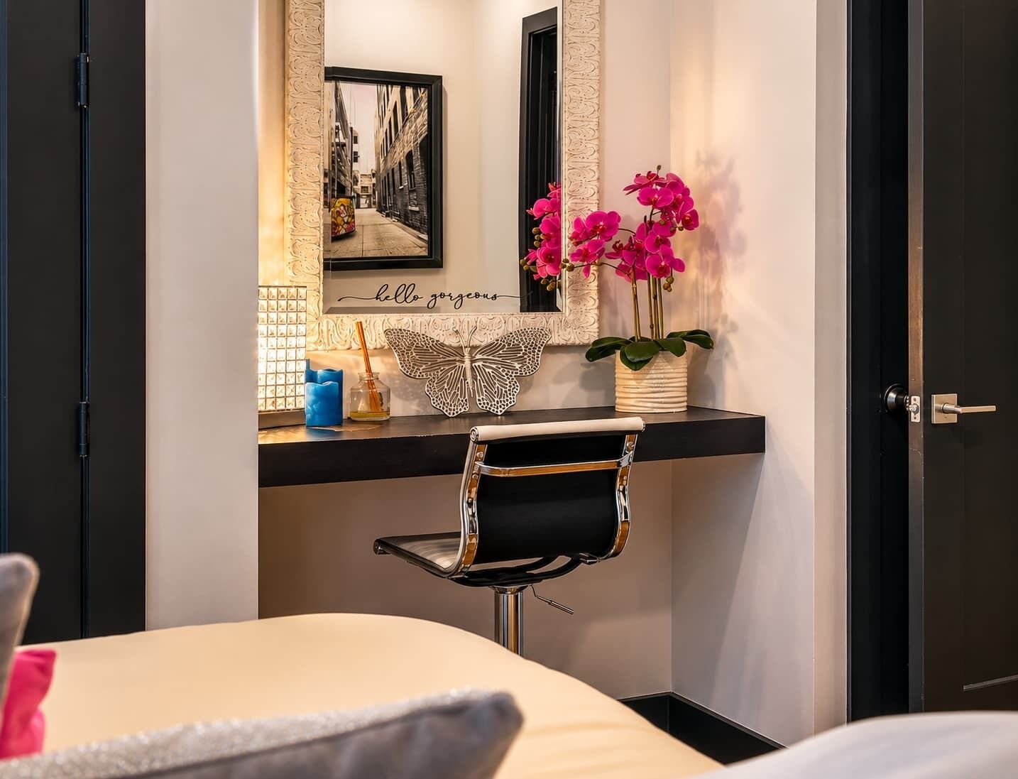 A hotel room with a bed, a desk with a chair, a mirror, a framed picture, and a vase with flowers.