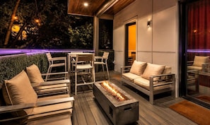 Eine Terrasse im Freien mit moderner Möbel, einer Feuerstelle und stimmungsvoller Beleuchtung.