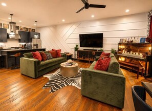 Ein modernes Wohnzimmer mit einem Flachbildfernseher, zwei grünen Sofas mit roten Kissen, einem Holztisch und einer Bar mit Flaschen.