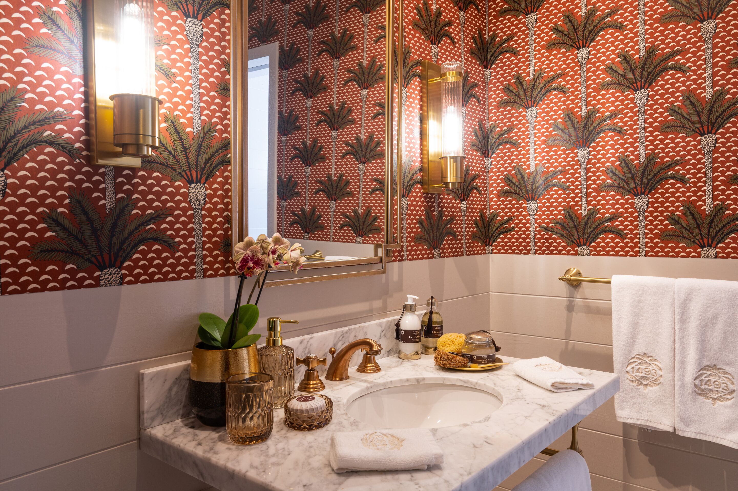 Un baño con lavamanos de mármol, detalles dorados y papel tapiz estampado.