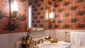A bathroom with a marble sink, gold fixtures, and a patterned wallpaper.