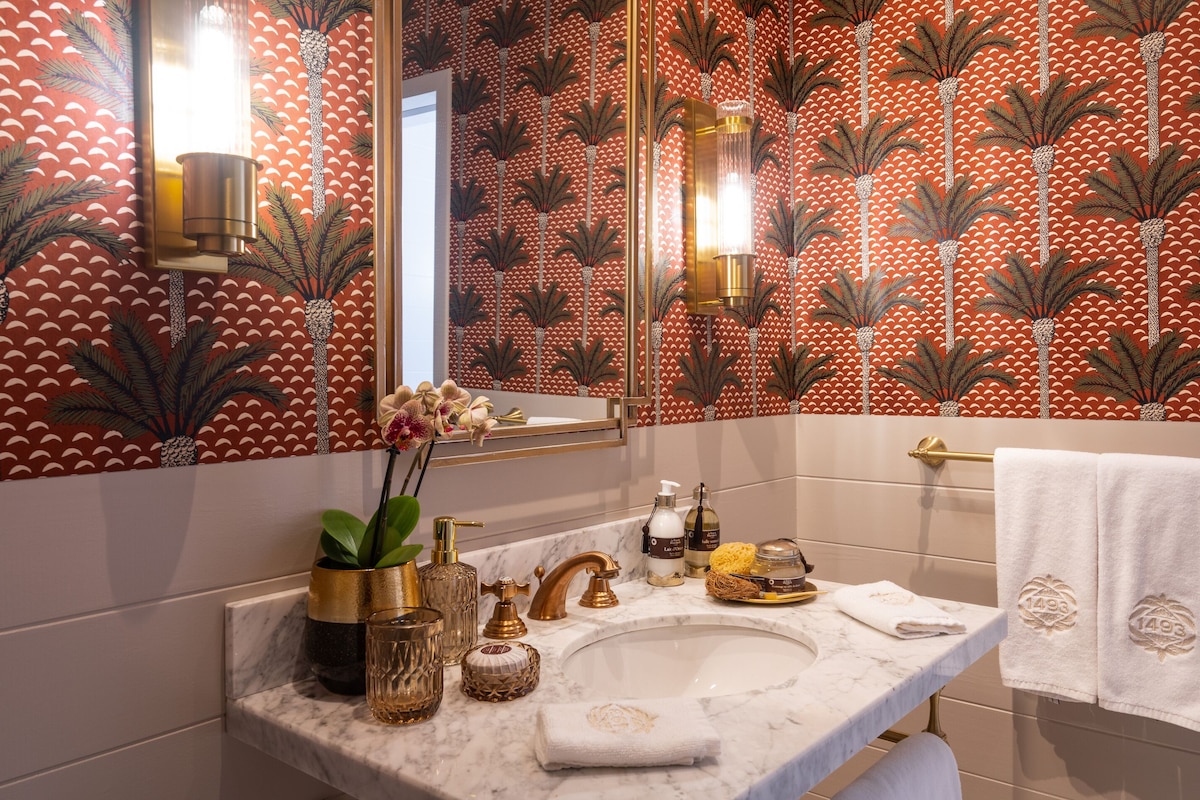 Une salle de bain avec un lavabo en marbre, des robinetteries dorées et un papier peint à motifs.