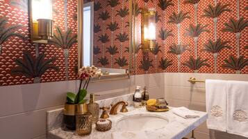 Un baño con lavamanos de mármol, detalles dorados y papel tapiz estampado.
