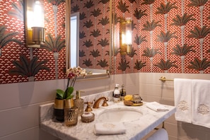 Une salle de bain avec un lavabo en marbre, des robinetteries dorées et un papier peint à motifs.