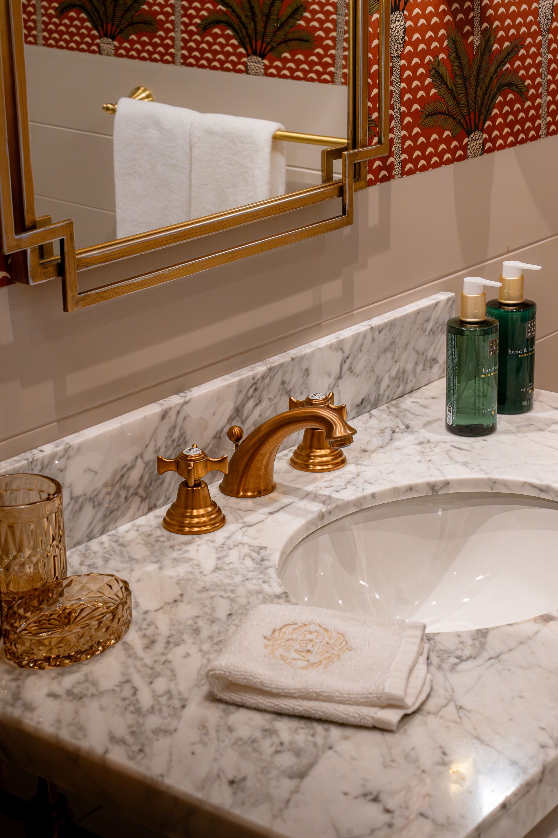 Un baño con lavamanos de mármol, grifos dorados y una toalla con diseño floral.