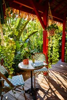 Un área de estar al aire libre con una mesa redonda y dos sillas, rodeada de abundante vegetación y una estructura roja.