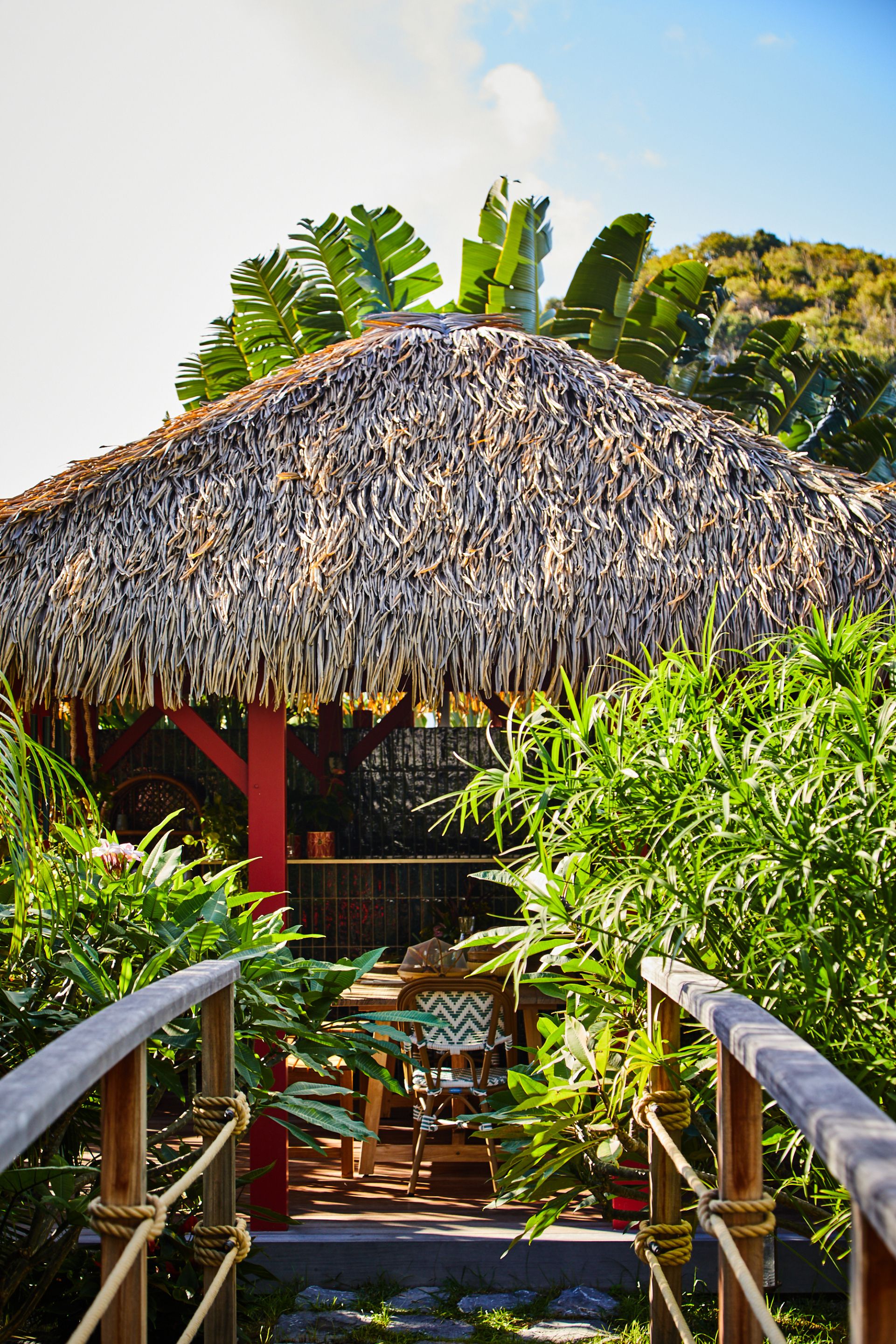A thatched-roof structure with a wooden staircase leading to a covered seating area.