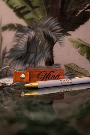 A wooden name block with 'Nina' engraved, a pen with a gold tip, and a keychain with a leather pouch.