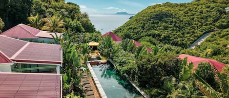 A resort with a swimming pool surrounded by lush greenery and red-roofed buildings.