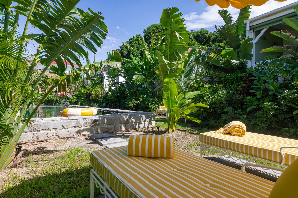 Ein Garten mit Pool, Steinmauern und gelb-weiß gestreifter Möbel.