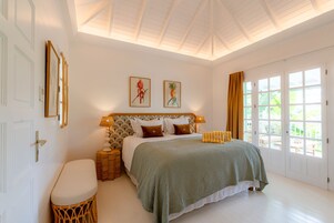 Un dormitorio con cama, mesitas de noche, una ventana y una puerta.