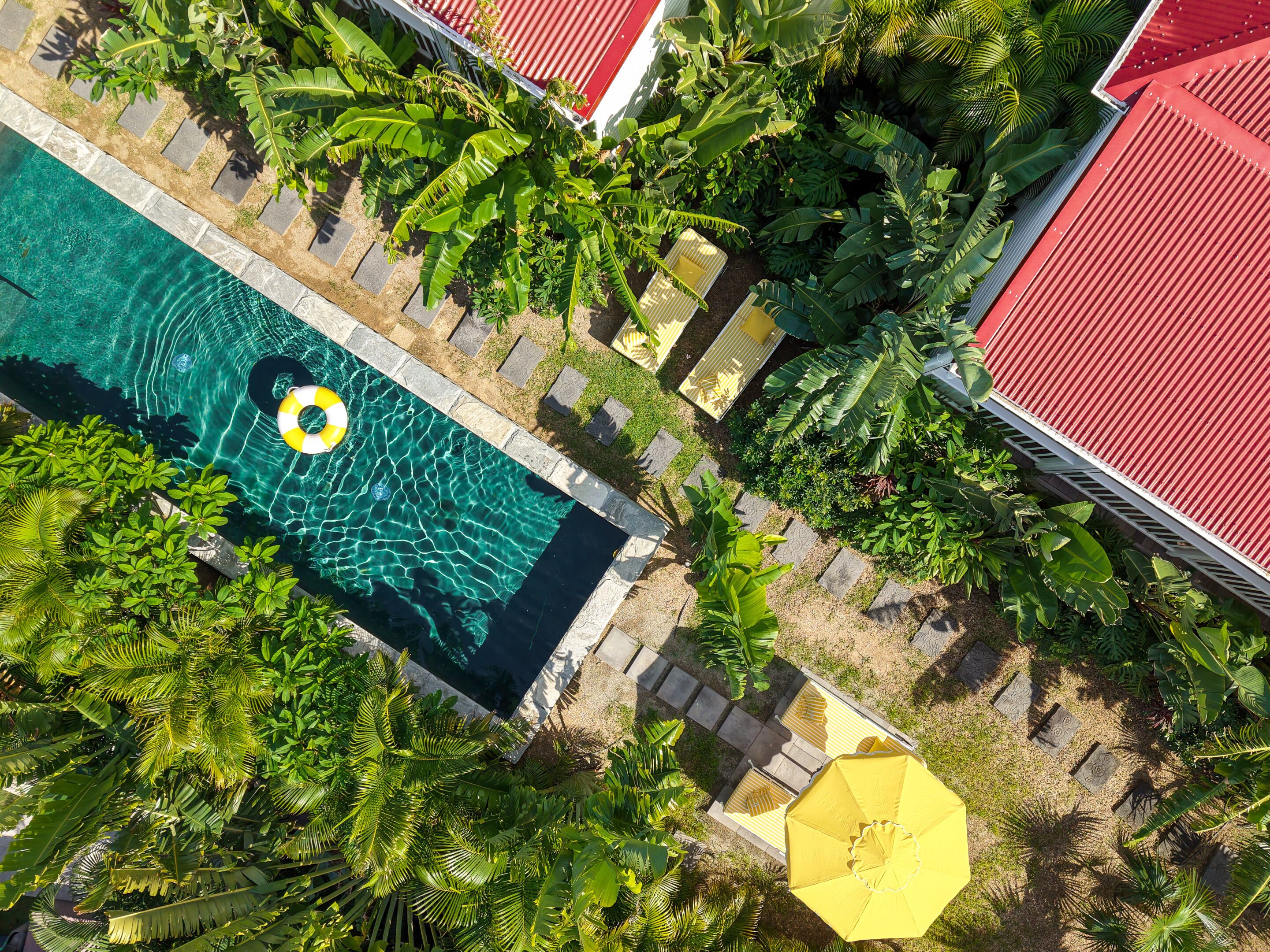 A swimming pool surrounded by lush greenery and red-roofed buildings.