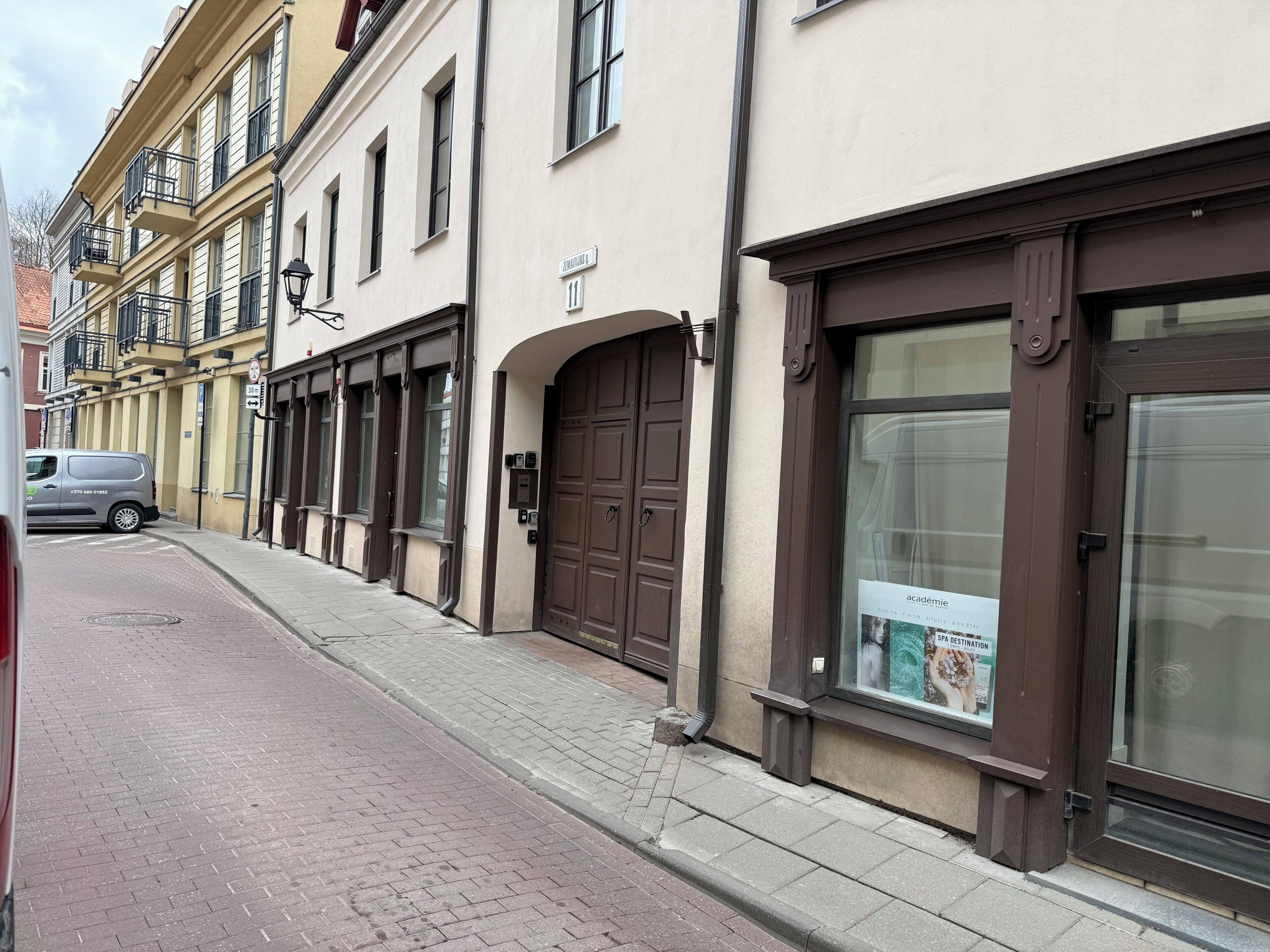 Straßenansicht eines Gebäudes mit einer großen braunen Tür, einem Schild mit der Nummer 11 und einem Plakat, das ein Wellnessziel bewirbt.