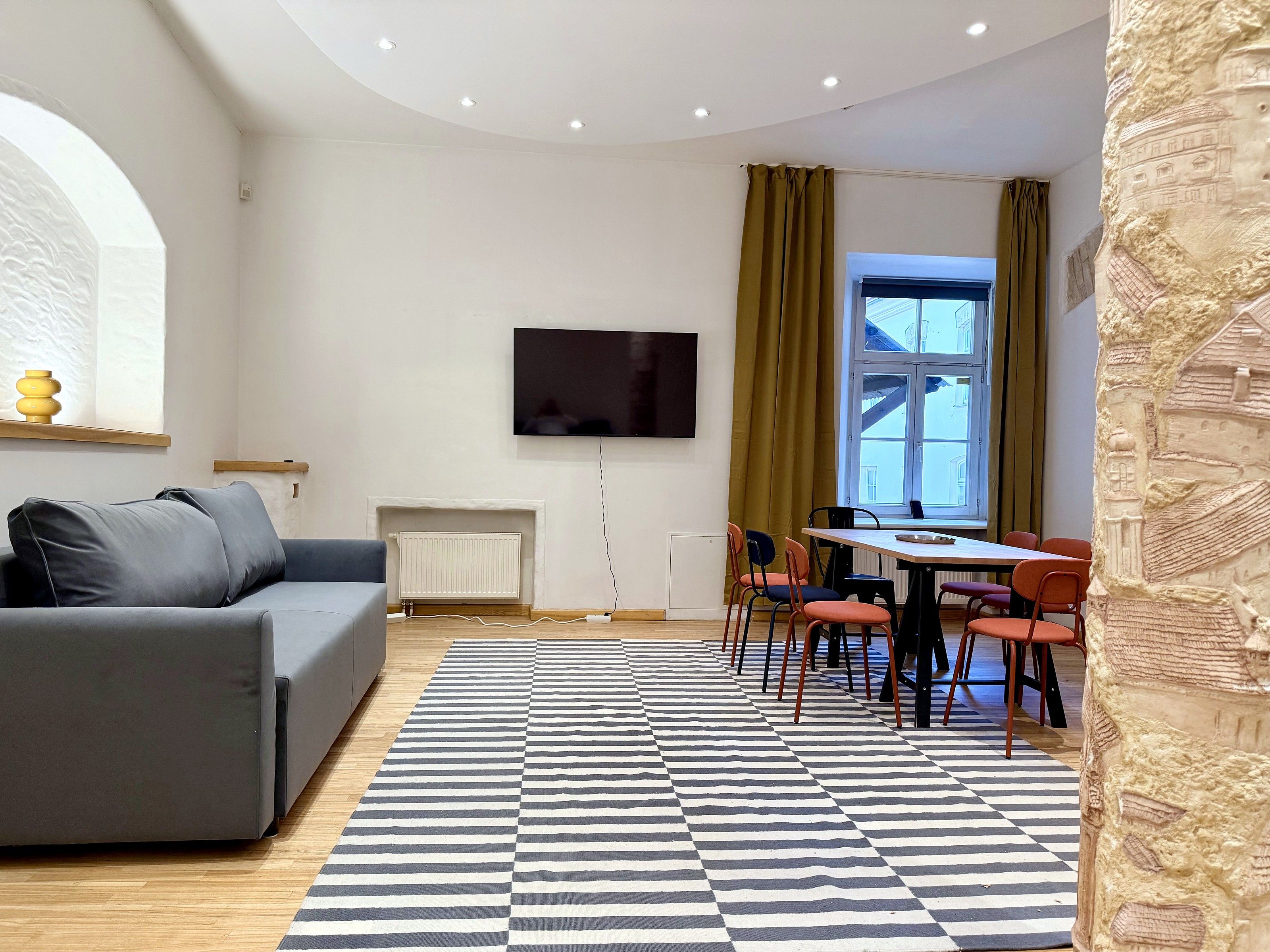 A modern living room with a grey sofa, a flat-screen TV, a fireplace, and a dining area with chairs.