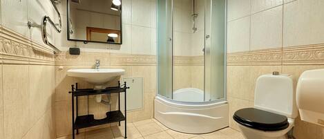 A bathroom with a sink, toilet, shower, and a mirror with lights.